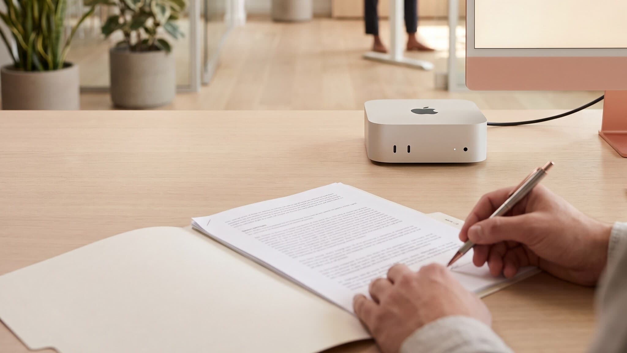 A prepared file being signed at a clear desk beside a Mac mini in a bright open office, human at the helm ai, Aceleron Intelligence