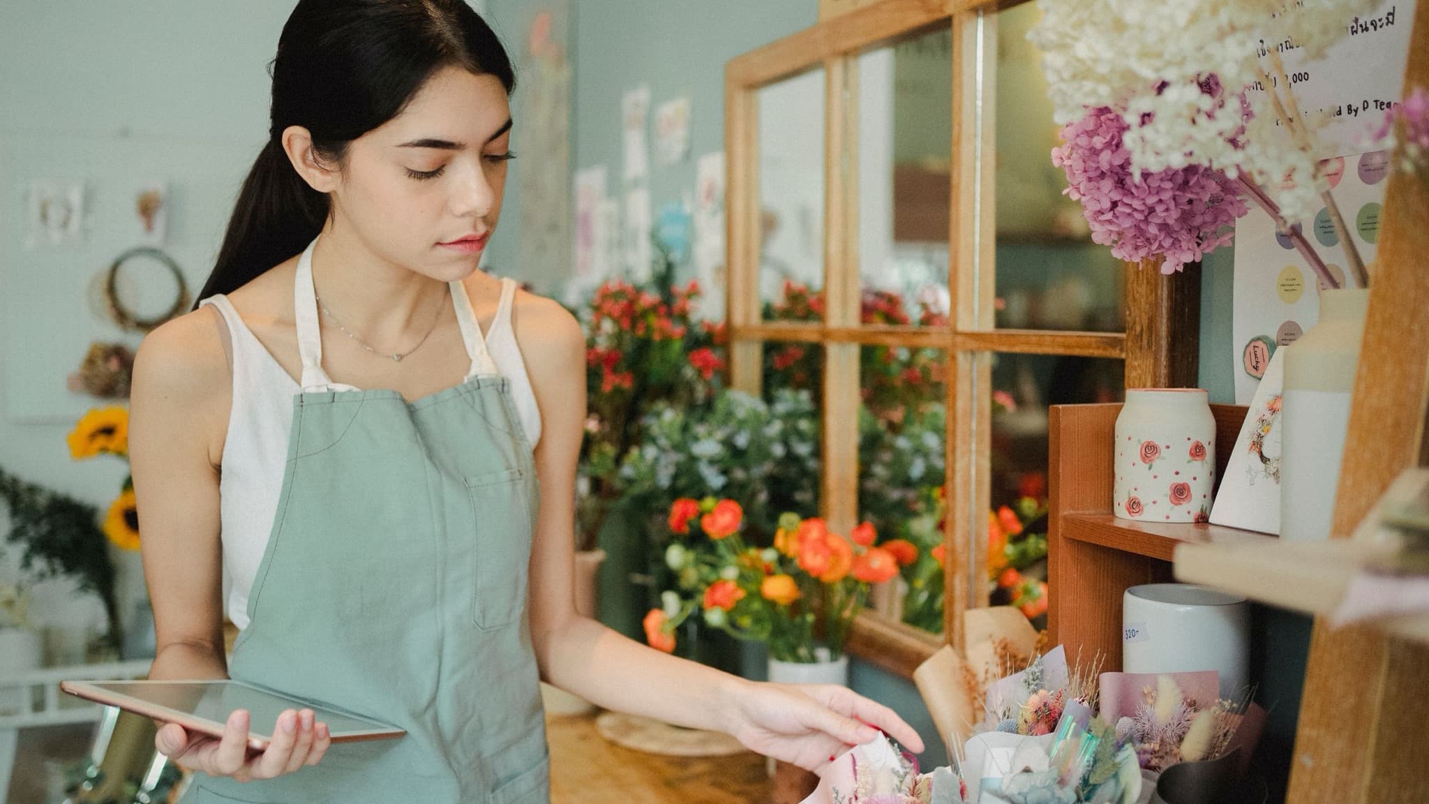 A small business owner at the counter of her bright flower shop checking a tablet, ai assistants recommending local businesses, Aceleron Intelligence